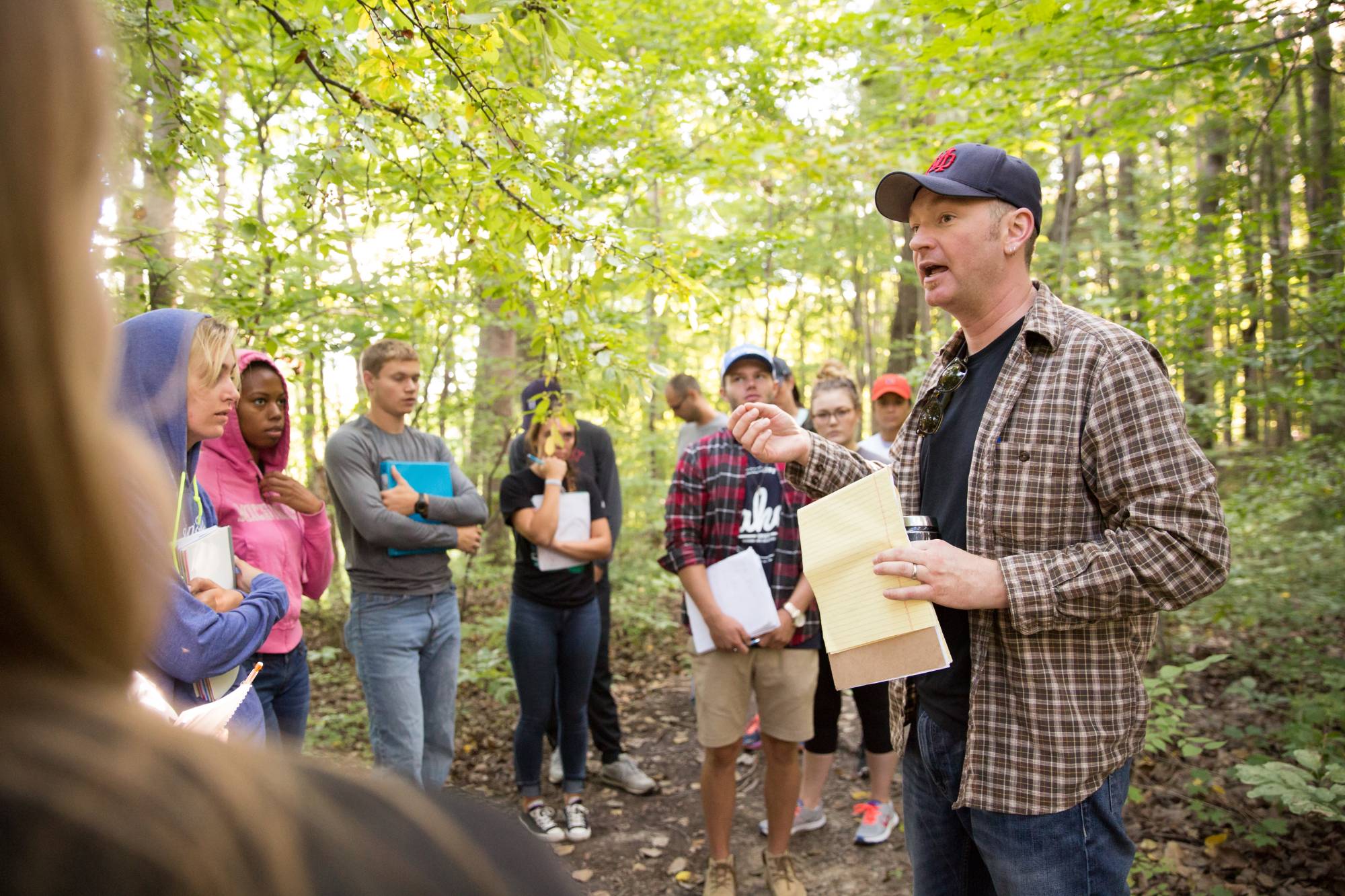 Integrated Science professor speaks to students outdoors; students are holding binders and papers.